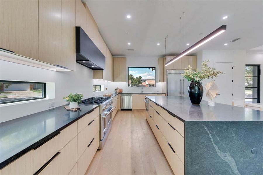 Kitchen with light brown cabinetry, high quality appliances, light wood-type flooring, and extractor fan