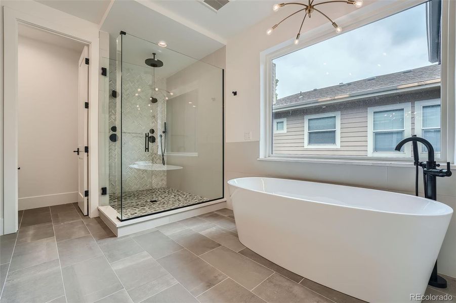 Spa inspired primary bath featuring free-standing soaking tub, multi-head shower, heated tile floors, dual vanities.