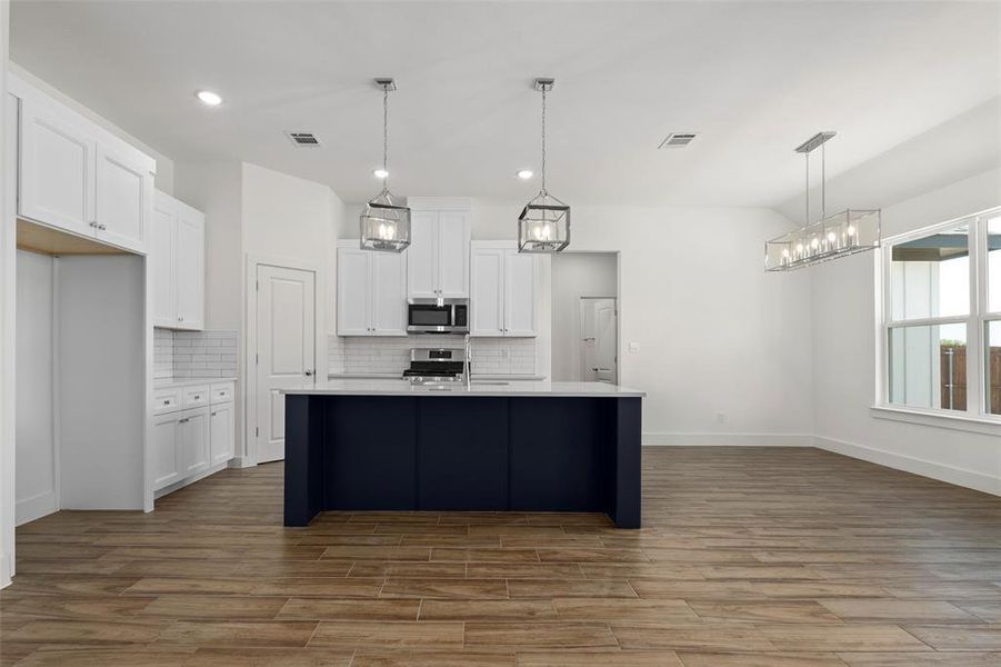 Kitchen with white cabinetry, tasteful backsplash, gas stove, pendant lighting, and a center island with sink