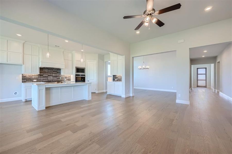 Kitchen with hanging light fixtures, a center island with sink, light hardwood / wood-style floors, and appliances with stainless steel finishes