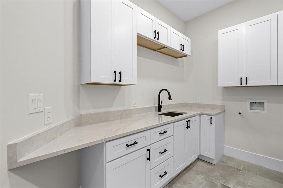 Kitchen with light tile patterned floors, light stone countertops, sink, and white cabinetry