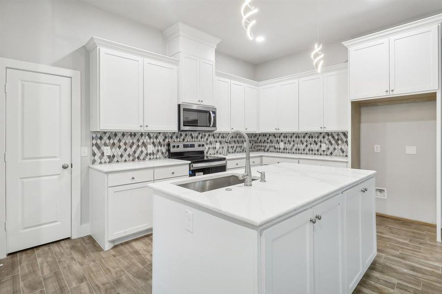 Kitchen featuring an island with sink, pendant lighting, stainless steel appliances, and white cabinets