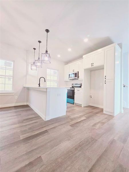 Kitchen featuring white cabinets, kitchen peninsula, decorative light fixtures, appliances with stainless steel finishes, and light hardwood / wood-style floors