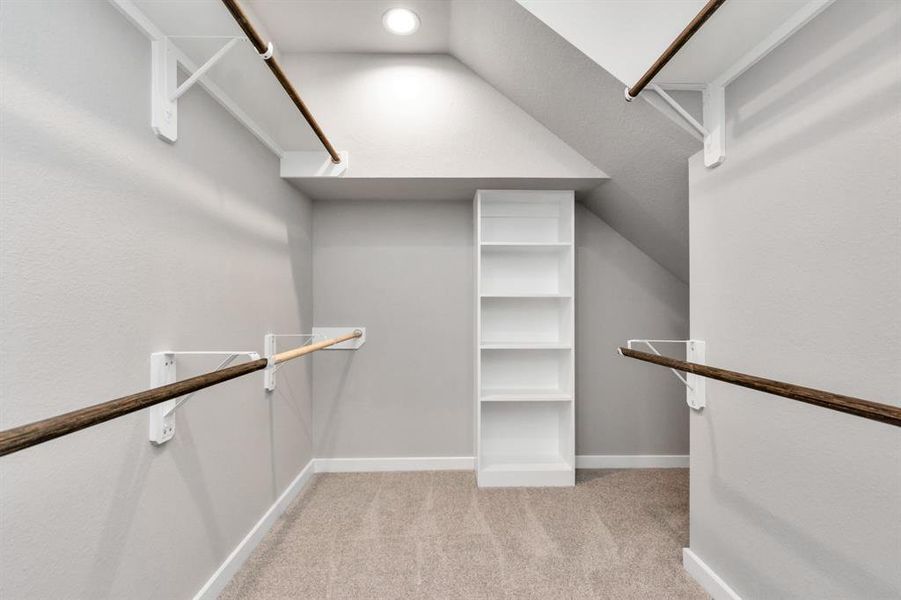 Experience luxury in this spacious walk-in closet with high ceilings and plush carpet. Warm paint tones, built-in shelving, and dark finishes create a contemporary and functional retreat. Sample photo of completed home with similar floor plan. As-built interior colors and selections may vary.