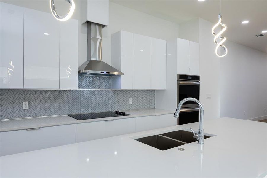 Kitchen featuring backsplash, cooktop, wall chimney exhaust hood, white cabinets, and sink