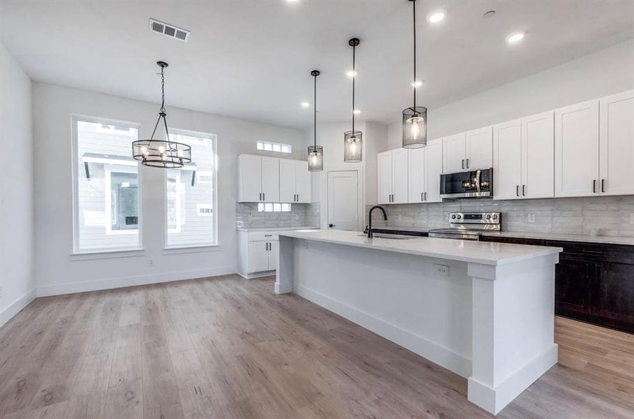 Kitchen featuring pendant lighting, light hardwood / wood-style flooring, stainless steel appliances, an island with sink, and decorative backsplash