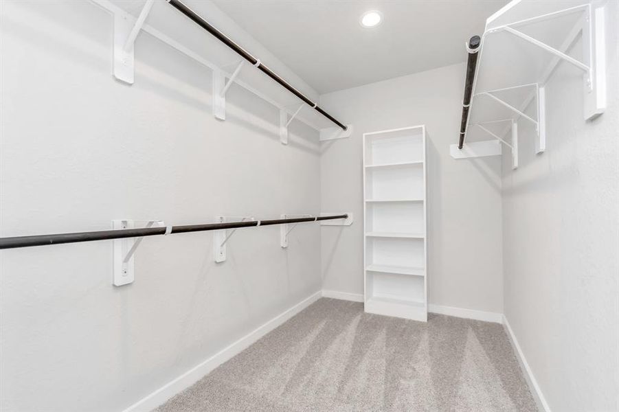 Immerse yourself in the lap of luxury within this roomy walk-in closet boasting high ceilings and plush carpeting. Let the inviting ambiance of warm paint tones surround you, make use of the practicality of built-in shelving, and revel in the contemporary and functional escape enriched by dark finishes. Sample photo of completed home with similar floor plan. As-built interior colors and selections may vary.