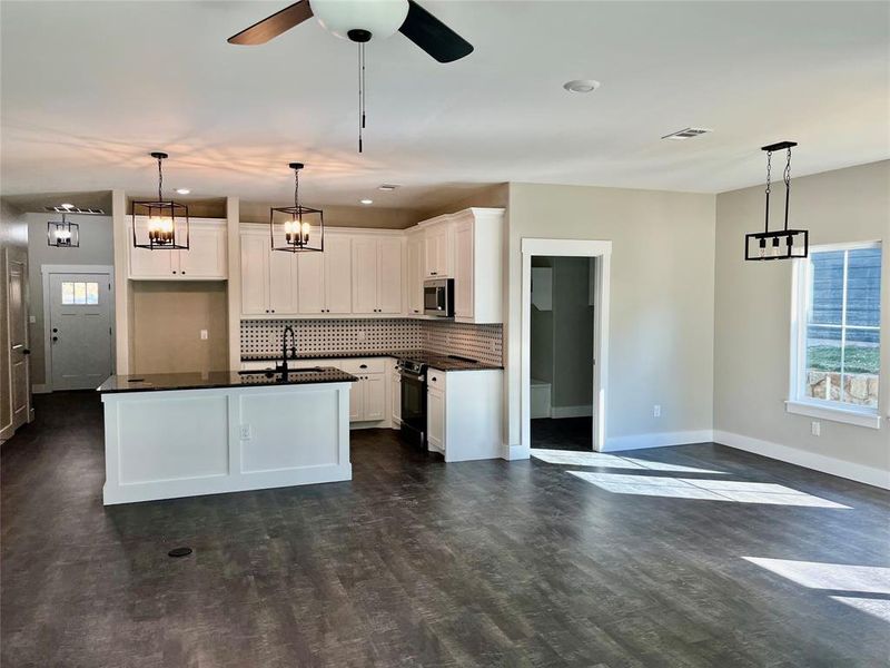 Kitchen featuring white cabinetry, a kitchen island with sink, dark wood-type flooring, and pendant lighting