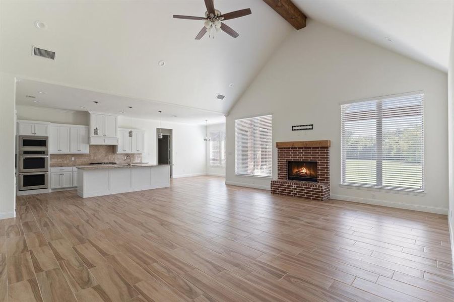 Unfurnished living room featuring beamed ceiling, sink, a fireplace, high vaulted ceiling, and ceiling fan