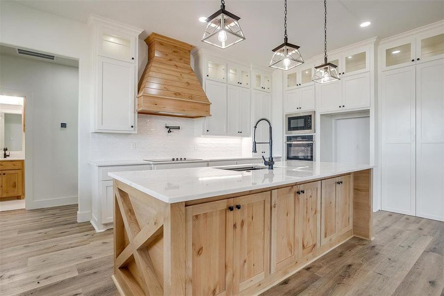 Kitchen with premium range hood, stainless steel oven, a kitchen island with sink, and sink