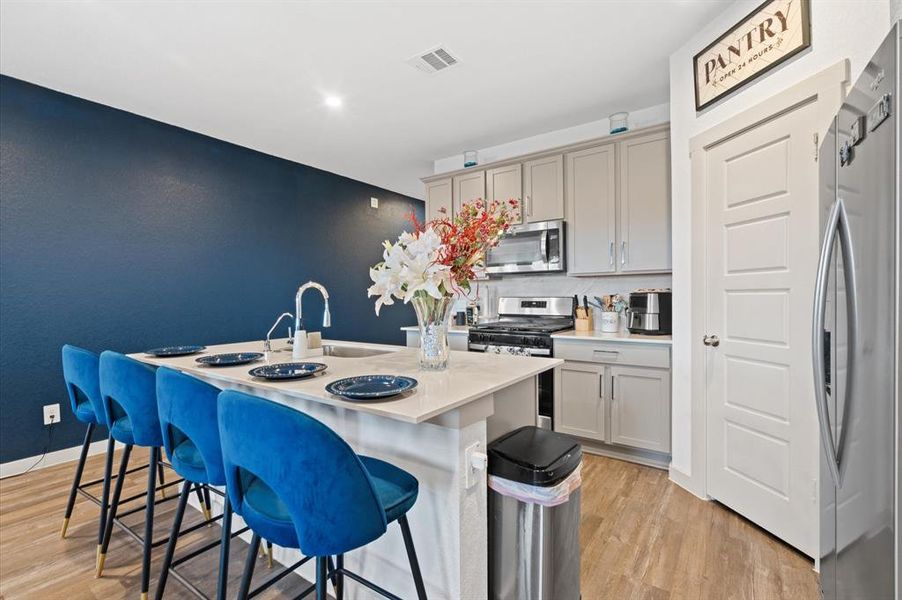 This is a modern kitchen featuring stainless steel appliances, white cabinetry, a deep blue accent wall, and a breakfast bar. There's also a designated pantry area for additional storage. Approximate Measurements: 17x11