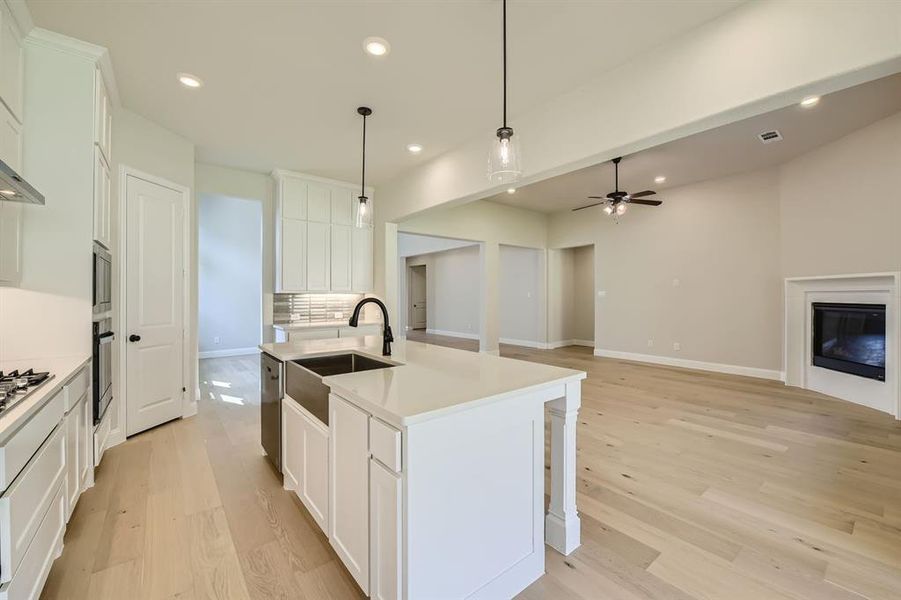 Kitchen with light wood-type flooring, white cabinets, and a center island with sink