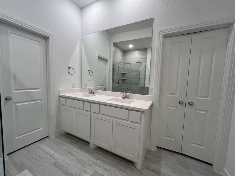 Bathroom featuring a shower with door, large vanity, and double sink