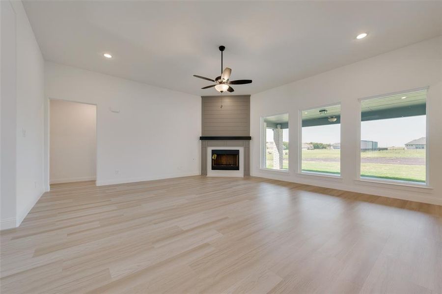 Unfurnished living room with a fireplace, ceiling fan, and light wood-type flooring