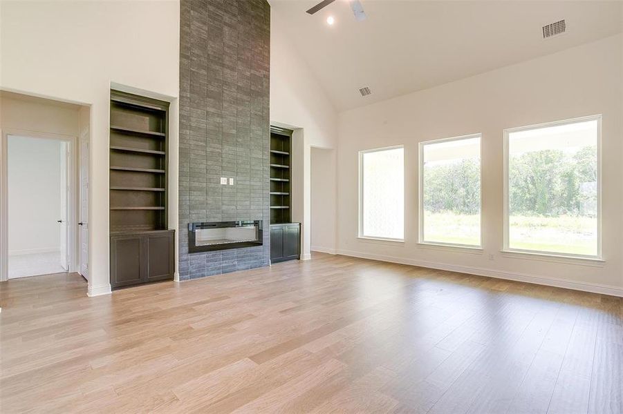 Unfurnished living room featuring light hardwood / wood-style flooring, a fireplace, built in shelves, high vaulted ceiling, and ceiling fan