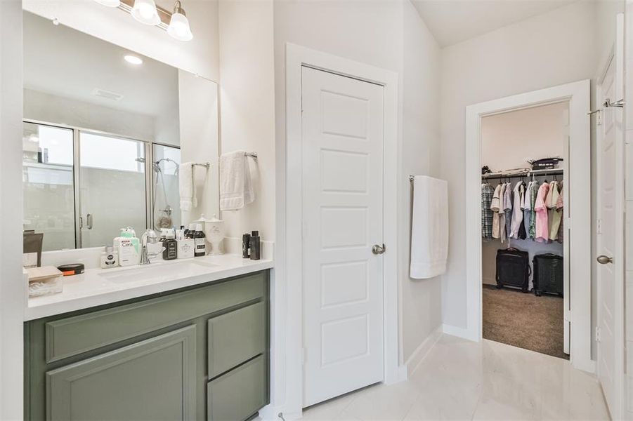 This is a modern bathroom with dual vanities, a large mirror, and good lighting. It also features a walk-in closet.