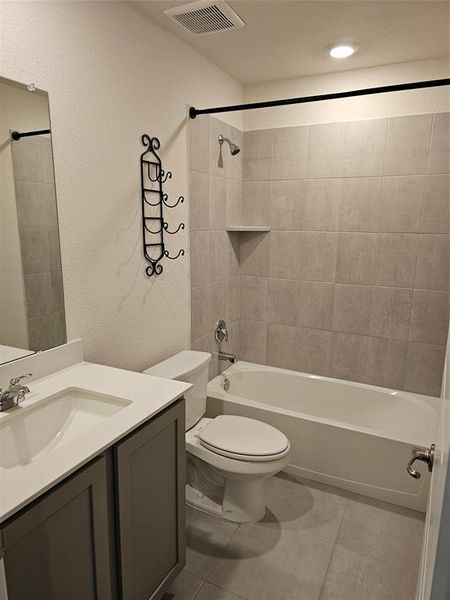 Full bathroom featuring vanity, tiled shower / bath combo, toilet, and tile patterned flooring