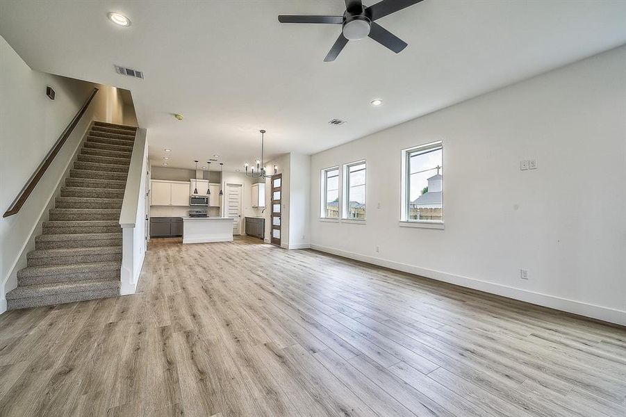 Unfurnished living room with light wood-type flooring and ceiling fan with notable chandelier