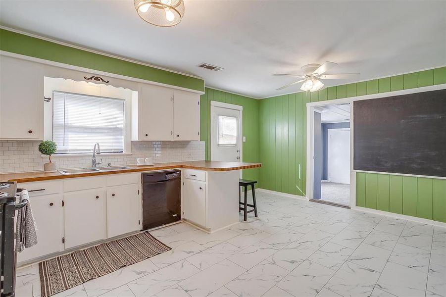 Kitchen with plenty of natural light, dishwasher, wooden walls, and white cabinets