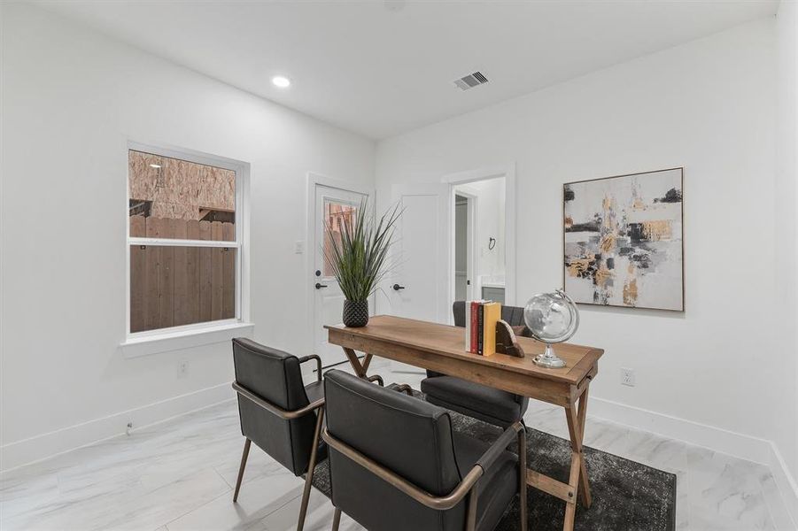 Modern, bright office space highlighted with clean lines, a large window for natural light, recessed lighting and sleek, marble-like tile flooring.