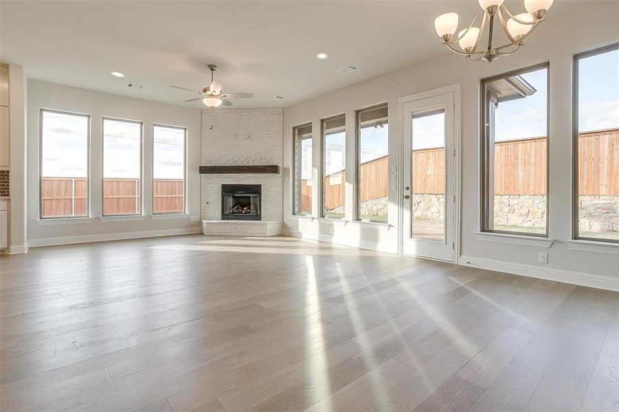 Unfurnished living room featuring a large fireplace, ceiling fan with notable chandelier, brick wall, and light wood-type flooring