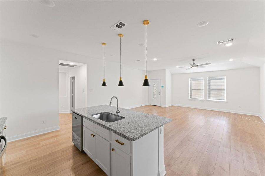 Kitchen featuring a center island with sink, hanging light fixtures, light stone counters, light hardwood / wood-style floors, and sink