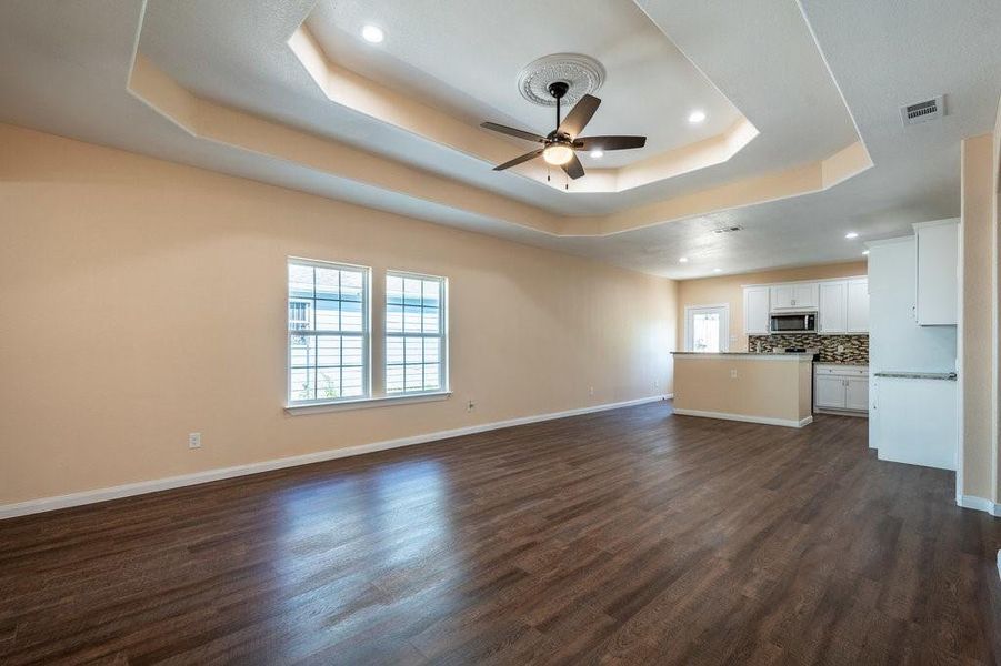 Unfurnished living room featuring ceiling fan, dark hardwood / wood-style floors, and a tray ceiling