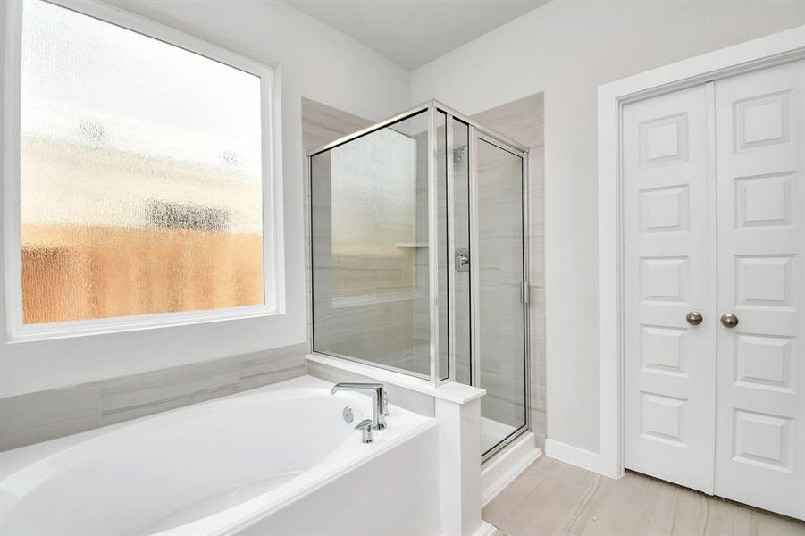 Experience a spa-like escape right in the heart of your primary bathroom. The expansive walk-in shower, surrounded by tile, and the distinctive garden tub with unique accents elevate your daily routine. The sophisticated vanity, featuring double sinks, dark-colored countertops, contemporary hardware, and bright recessed lighting, adds both style and functionality to the space. Sample photo of completed home with similar floor plan. Actual colors and selections may vary.