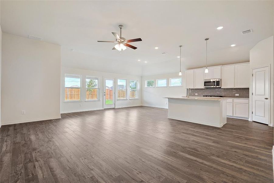 Kitchen featuring decorative light fixtures, dark wood-type flooring, tasteful backsplash, and a kitchen island with sink