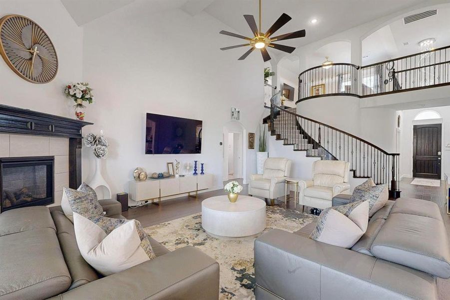 Living room with wood-type flooring, a tile fireplace, ceiling fan, beamed ceiling, and high vaulted ceiling