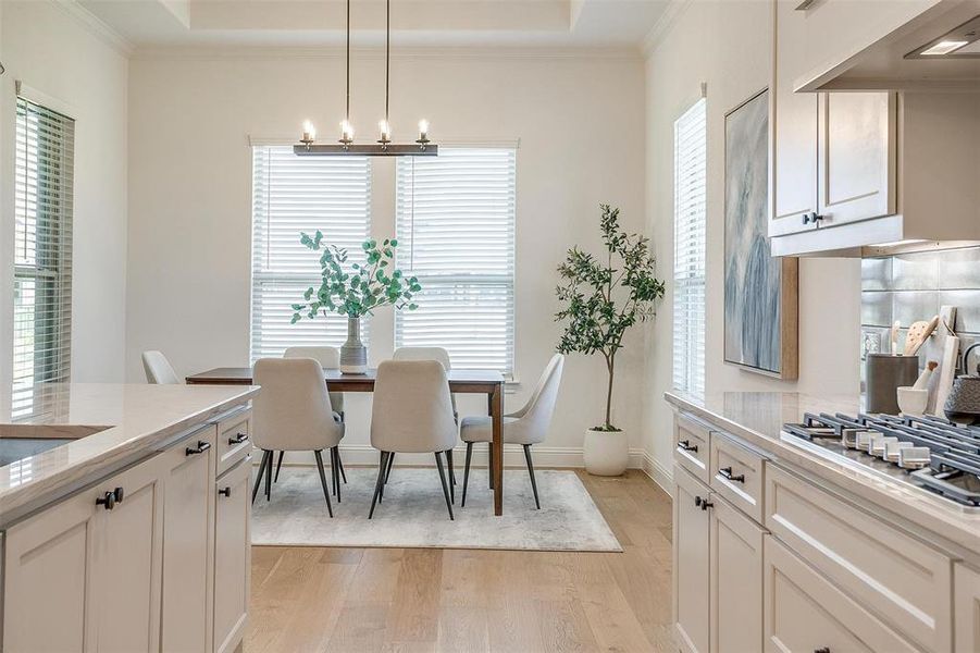 Dining space with ornamental molding, a tray ceiling, light wood-type flooring, and an inviting chandelier