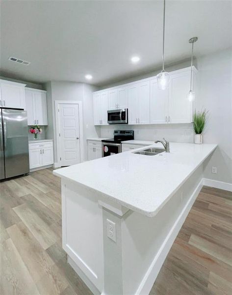 Kitchen featuring appliances with stainless steel finishes, hanging light fixtures, sink, and kitchen peninsula