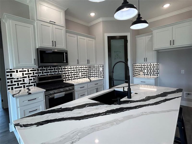 Kitchen featuring light stone countertops, stainless steel appliances, white cabinetry, a center island with sink, and decorative light fixtures