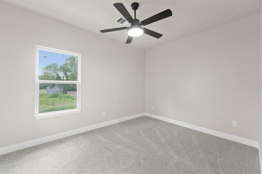 This is a bright, freshly painted room featuring a large window for natural light, carpet flooring, and a modern ceiling fan.