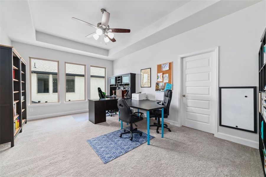 This is a bright and spacious Game Room featuring a tray ceiling with a ceiling fan, plush carpeting, and ample natural light from three large windows.