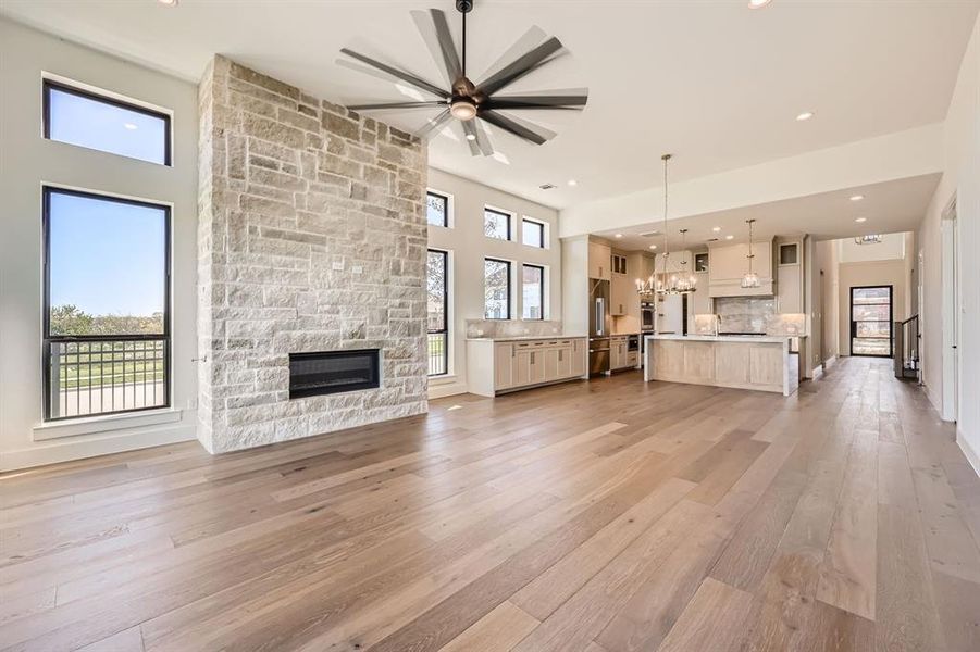 Unfurnished living room featuring ceiling fan with notable chandelier, light hardwood / wood-style floors, plenty of natural light, and a stone fireplace