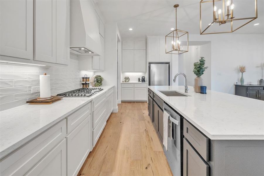 Kitchen featuring sink, a kitchen island with sink, hanging light fixtures, and custom exhaust hood