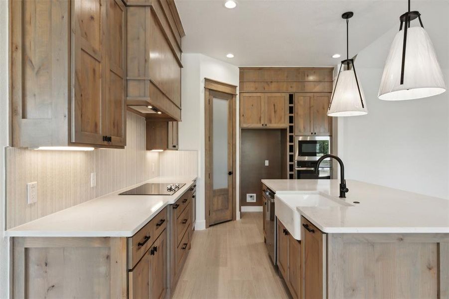 Kitchen featuring stainless steel appliances, sink, light hardwood / wood-style floors, decorative light fixtures, and a kitchen island with sink