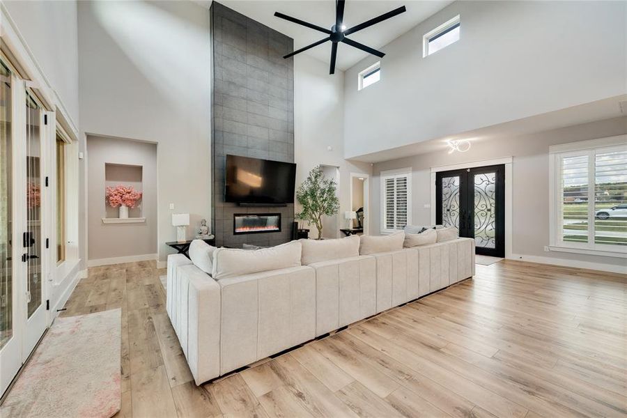 Living room featuring french doors, a high ceiling, light wood-type flooring, and a fireplace