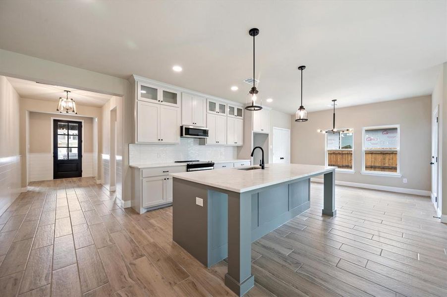 Kitchen featuring stainless steel appliances, white cabinets, sink, decorative light fixtures, and a kitchen island with sink