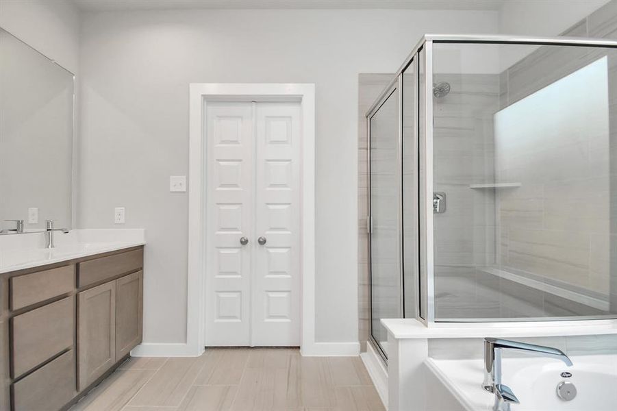 Delight in a spacious walk-in shower enveloped in stylish tile surround, unwind in a separate garden tub adorned with custom detailing, and elevate your daily routine at the elegant vanity, now equipped with double sinks, light countertops, modern hardware. Photo shown is example of completed home with similar plan.