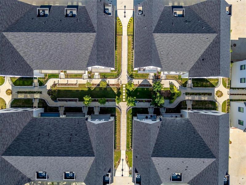 An aerial view of the luxury townhomes reveals a harmonious blend of modern architecture and lush landscaping. The townhomes are arranged in an elegant pattern, each unit showcasing stylish rooftops and private, gated front yards. The well-planned community layout includes winding pathways, green spaces, and vibrant communal areas, all contributing to a serene and upscale living environment. The overall scene exudes sophistication and meticulous attention to detail, offering a picturesque overview of this exclusive residential enclave.