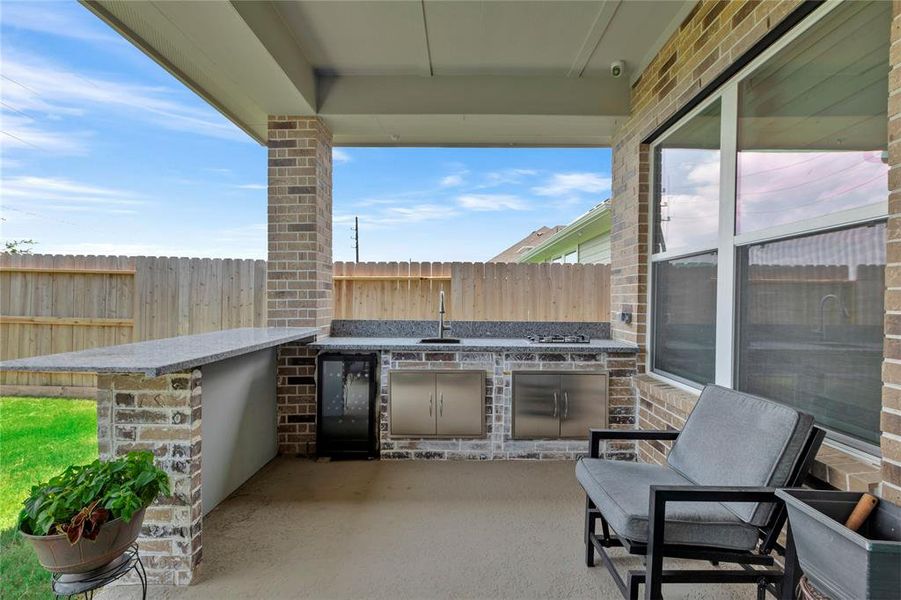 Outdoor Chef's Dream - Custom kitchen on the extended patio, featuring a mini-fridge space, sink, gas range, and bar area. Ideal for outdoor dining and entertaining.