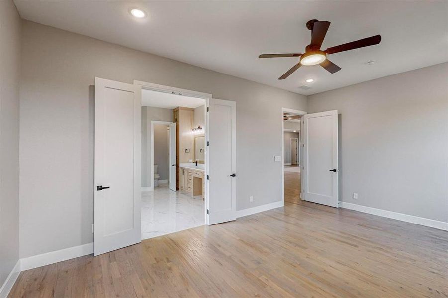 Unfurnished bedroom with ceiling fan, light wood-type flooring, and ensuite bath