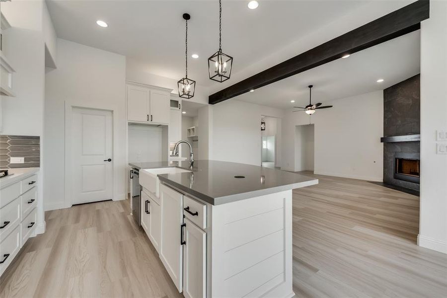 Kitchen featuring a kitchen island with sink, a tiled fireplace, ceiling fan with notable chandelier, and light hardwood / wood-style flooring