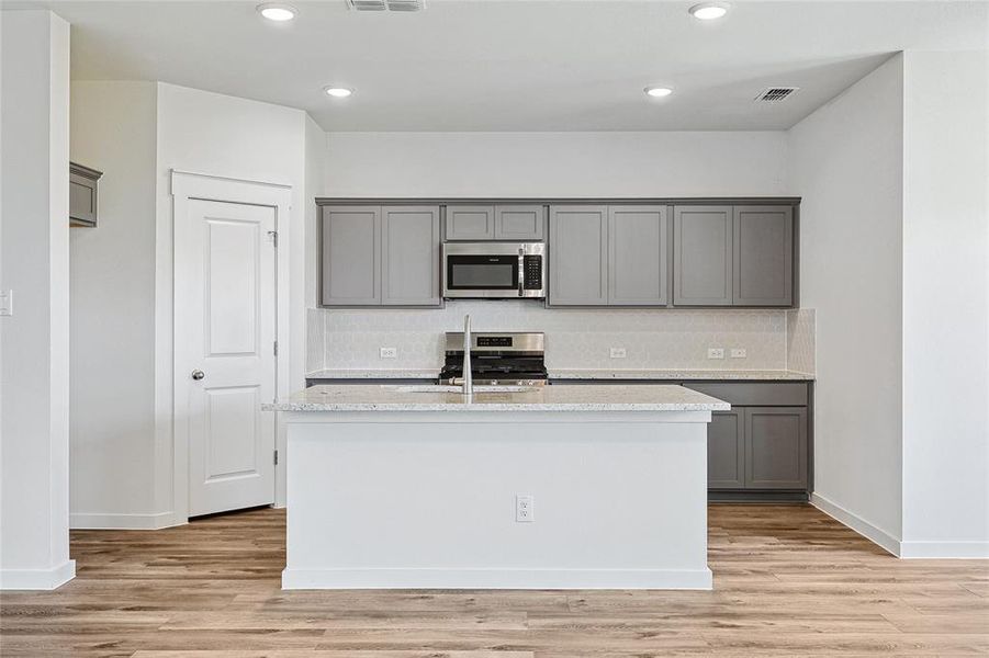 Kitchen with appliances with stainless steel finishes, light hardwood / wood-style flooring, a kitchen island with sink, and decorative backsplash