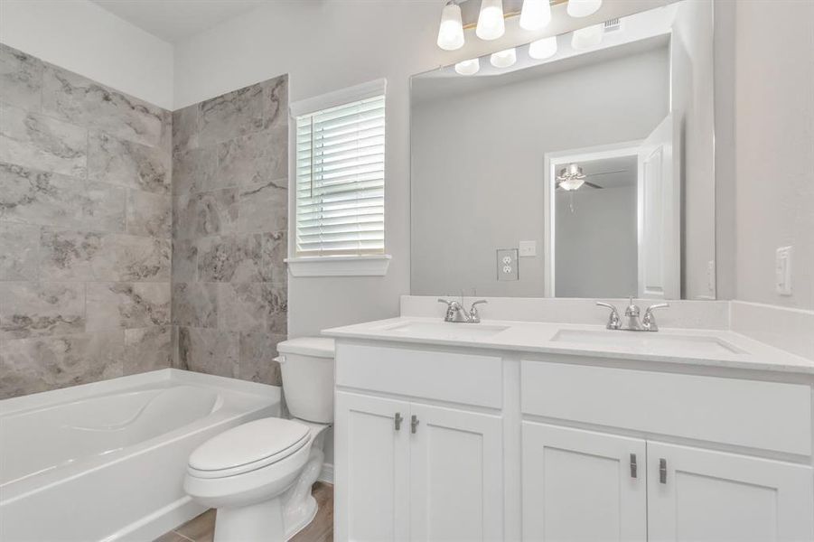 Start your day in this beautifully designed primary bathroom, featuring dual sinks and a spacious vanity with plenty of storage. The modern tile work in the shower/tub area adds a touch of elegance, while the large mirror and contemporary lighting fixtures enhance the room's bright, airy feel. This bathroom is both functional and stylish, offering the perfect blend of luxury and convenience. **This image is from another Saratoga Home with similar floor plan and finishes, not the June floorplan.**