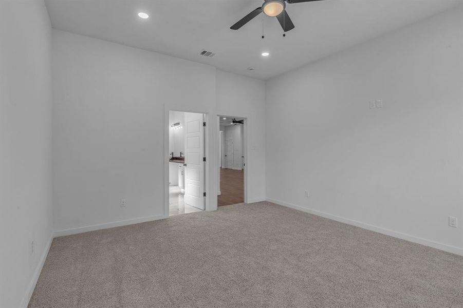 Unfurnished bedroom with connected bathroom, light colored carpet, and ceiling fan