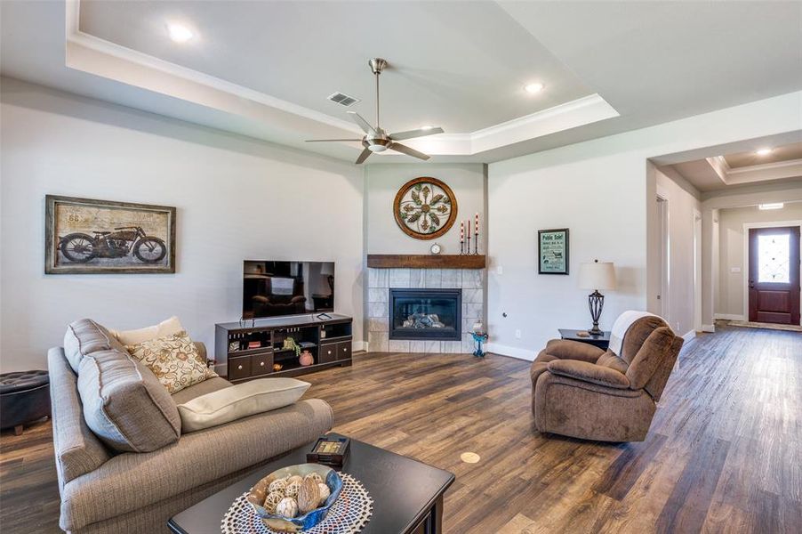 Living room featuring ceiling fan, a tray ceiling, a fireplace, and dark wood-type flooring