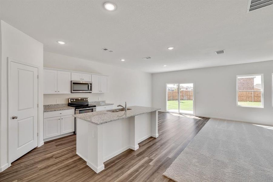 Kitchen featuring appliances with stainless steel finishes, white cabinetry, an island with sink, light hardwood / wood-style flooring, and sink